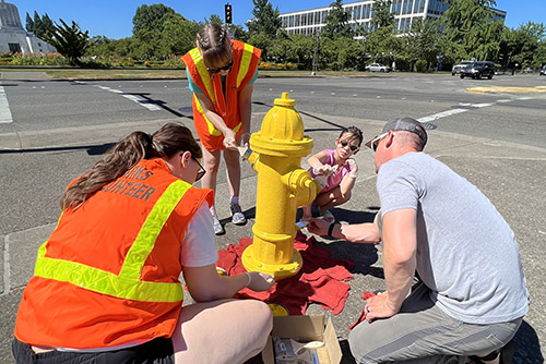 Three adults and one child paint a fire hydrant bright yellow