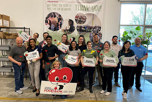 A group of smiling coworkers hold flowers and promotional signs while volunteering at the Central Pennsylvania Food Bank